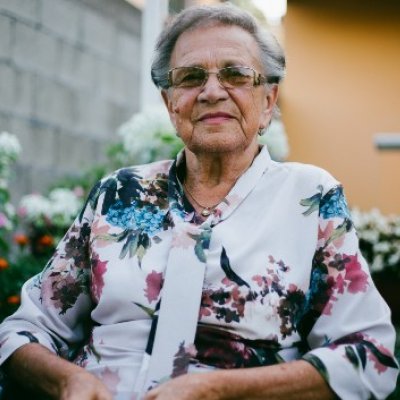 Elderly woman in floral shirt sits on walker.